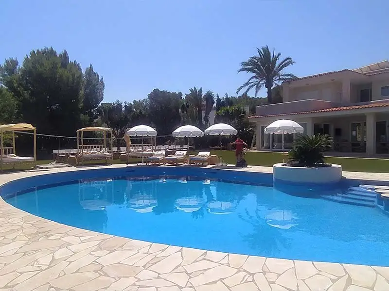 Piscine privée dans une villa rénovée à Ibiza avec chaises longues, parasols et jardin paysagé.