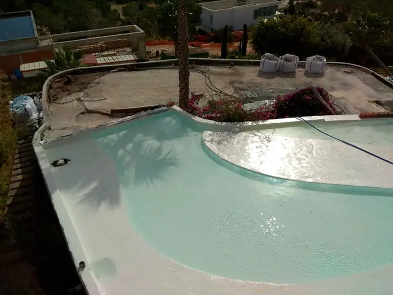 Piscine en rénovation à Ibiza avec film d'eau et solarium courbe, vue depuis la terrasse supérieure.